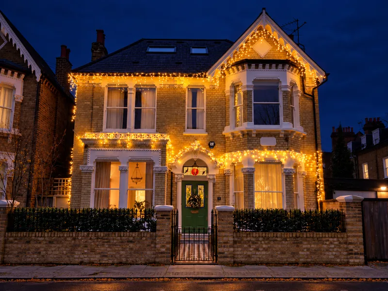 The same Battersea villa at dusk with warm white lights tracing the roofline and windows
